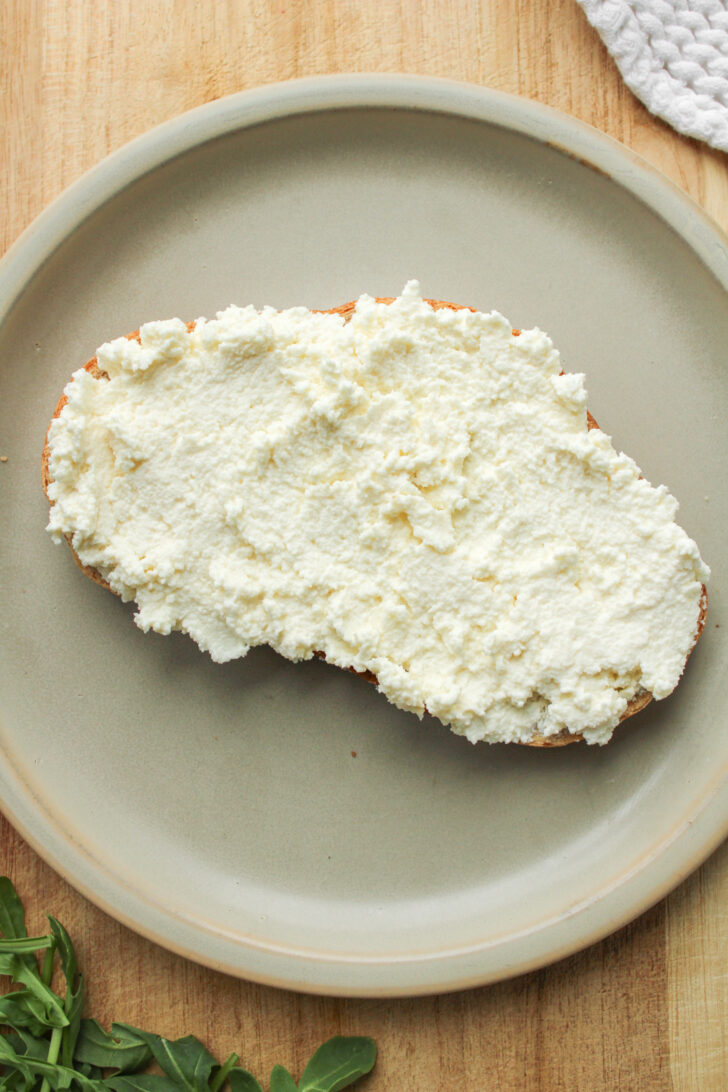 ricotta toast on a ceramic plate on top of a wooden cutting board
