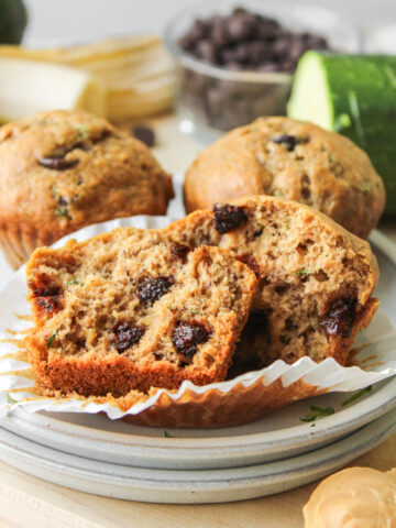 a banana zucchini chocolate chip muffin in half on top of stacked ceramic plates