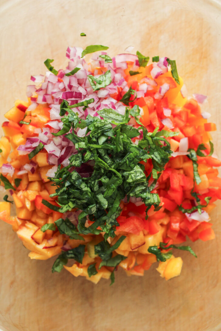 peach, mango, red onion and basil in a large glass bowl on top of a wooden cutting board