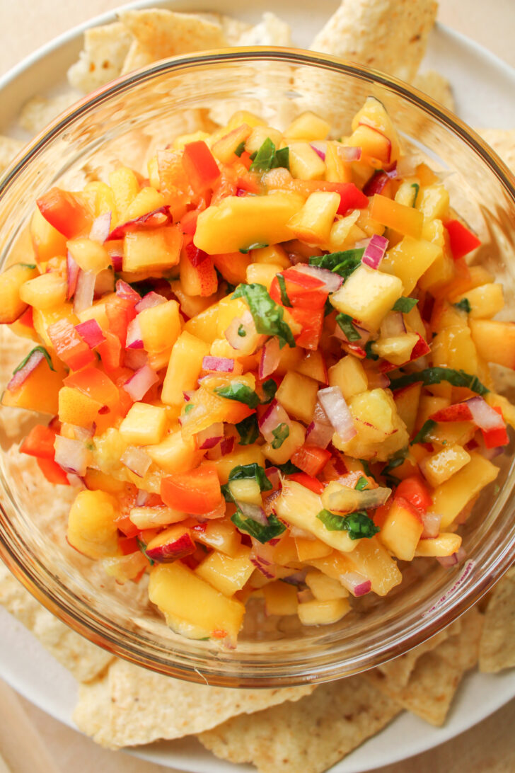 overhead shot of peach mango salsa in a glass bowl with tortilla chips surrounding it