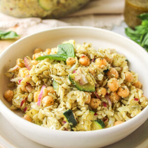 orzo pesto pasta salad in a white ceramic bowl with ingredients behind it
