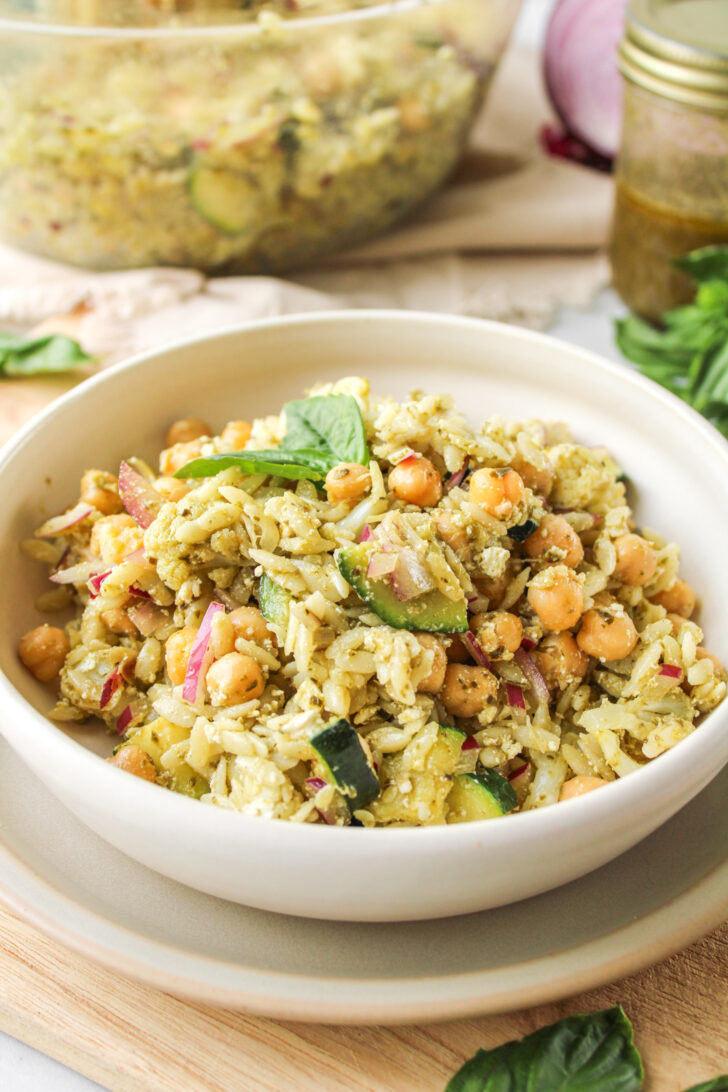 orzo pesto pasta salad in a white ceramic bowl with ingredients behind it