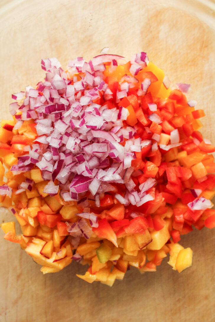 peach, mango and red onion in a large glass bowl on top of a wooden cutting board