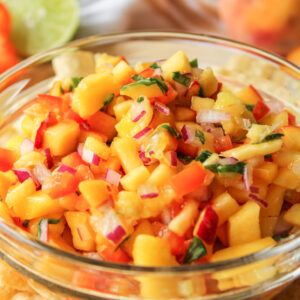 peach mango salsa in a glass bowl with tortilla chips surrounding it