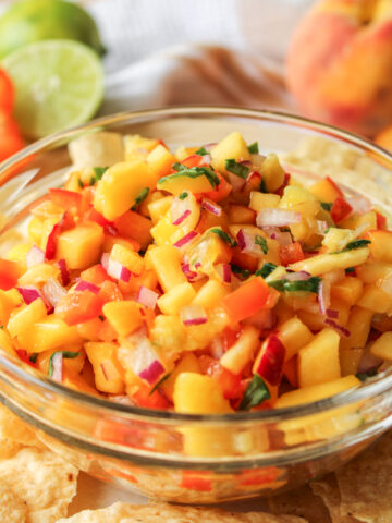 peach mango salsa in a glass bowl with tortilla chips surrounding it