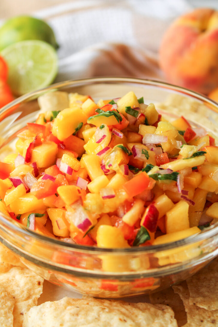 peach mango salsa in a glass bowl with tortilla chips surrounding it