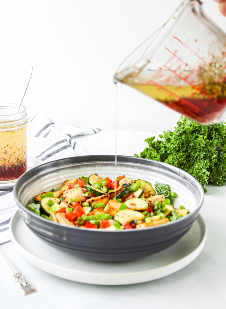 pouring the red wine vinegar dressing from a glass measuring cup onto a salad
