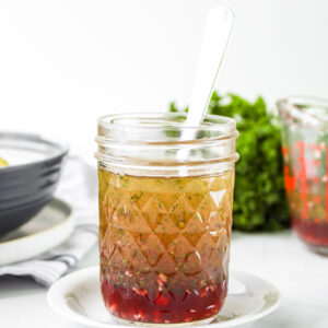 red wine vinegar salad dressing in a glass mason jar with a metal spoon in it on top of a small white plate