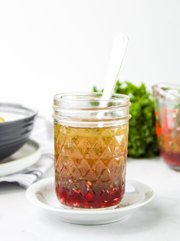 red wine vinegar salad dressing in a glass mason jar with a metal spoon in it on top of a small white plate