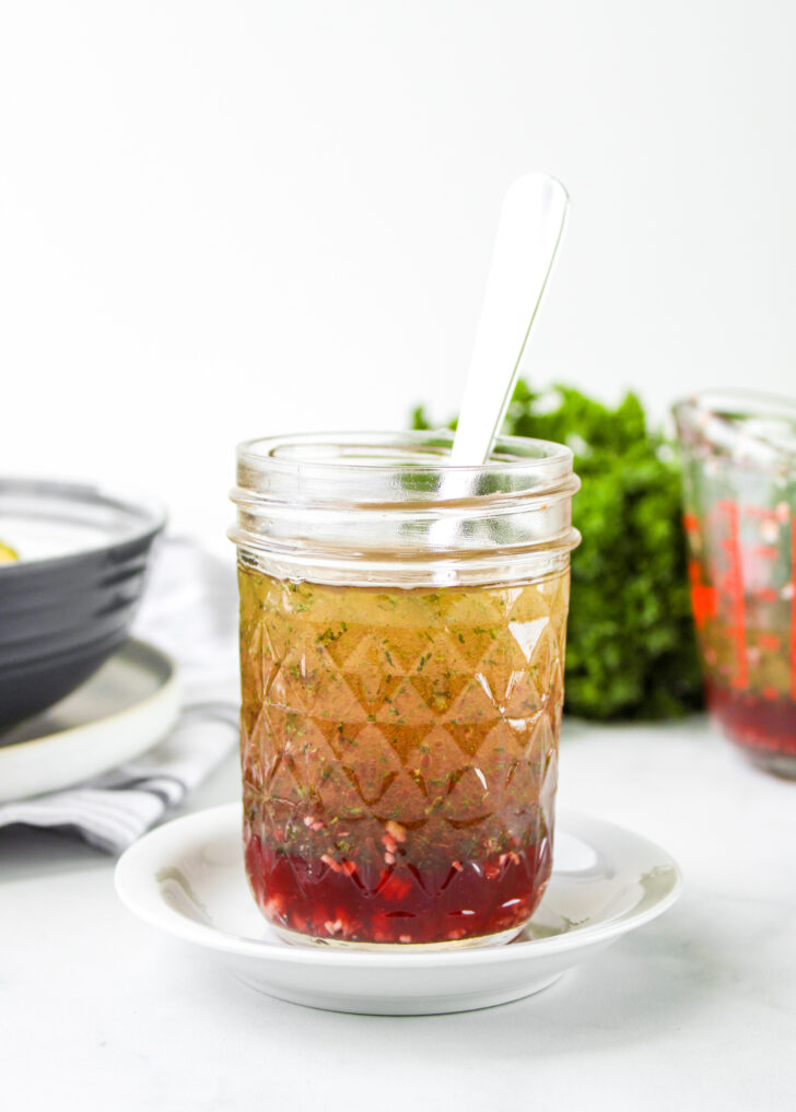 red wine vinegar salad dressing in a glass mason jar with a metal spoon in it on top of a small white plate