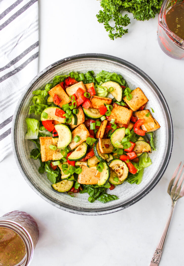 overheat shot of a salad with tofu and vegetables and the red wine vinaigrette on the side