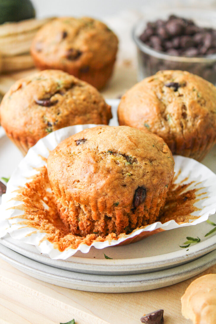 a banana zucchini chocolate chip muffins on top of the paper liner and muffins behind it