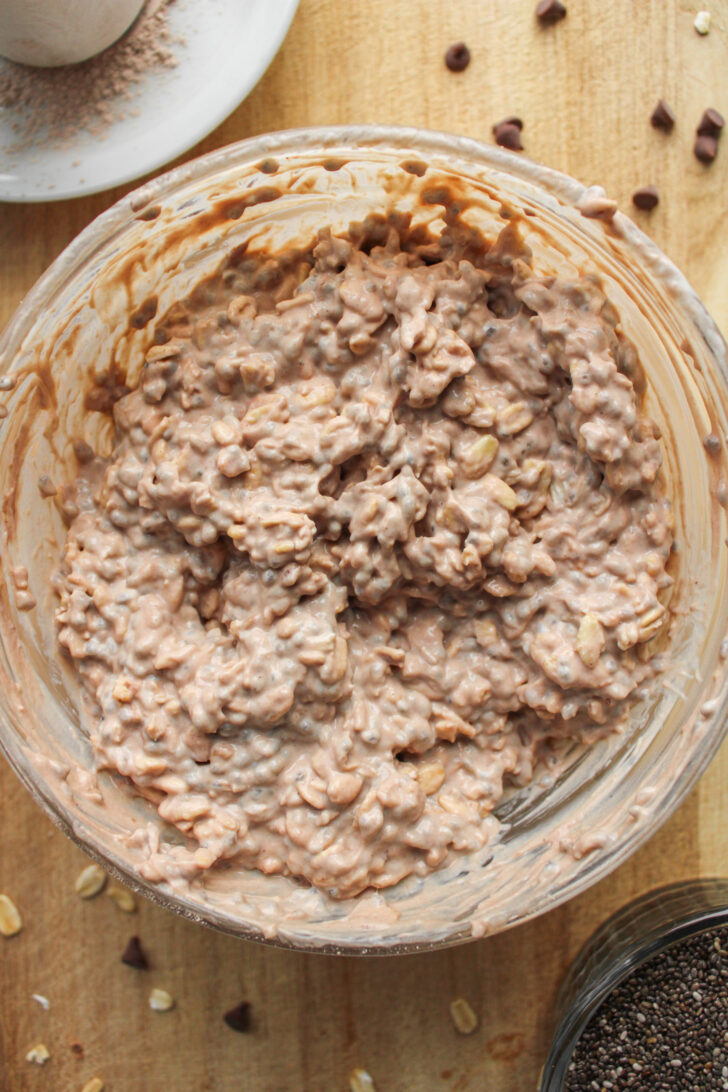 chocolate protein powder mixed into oat mixture in a glass bowl