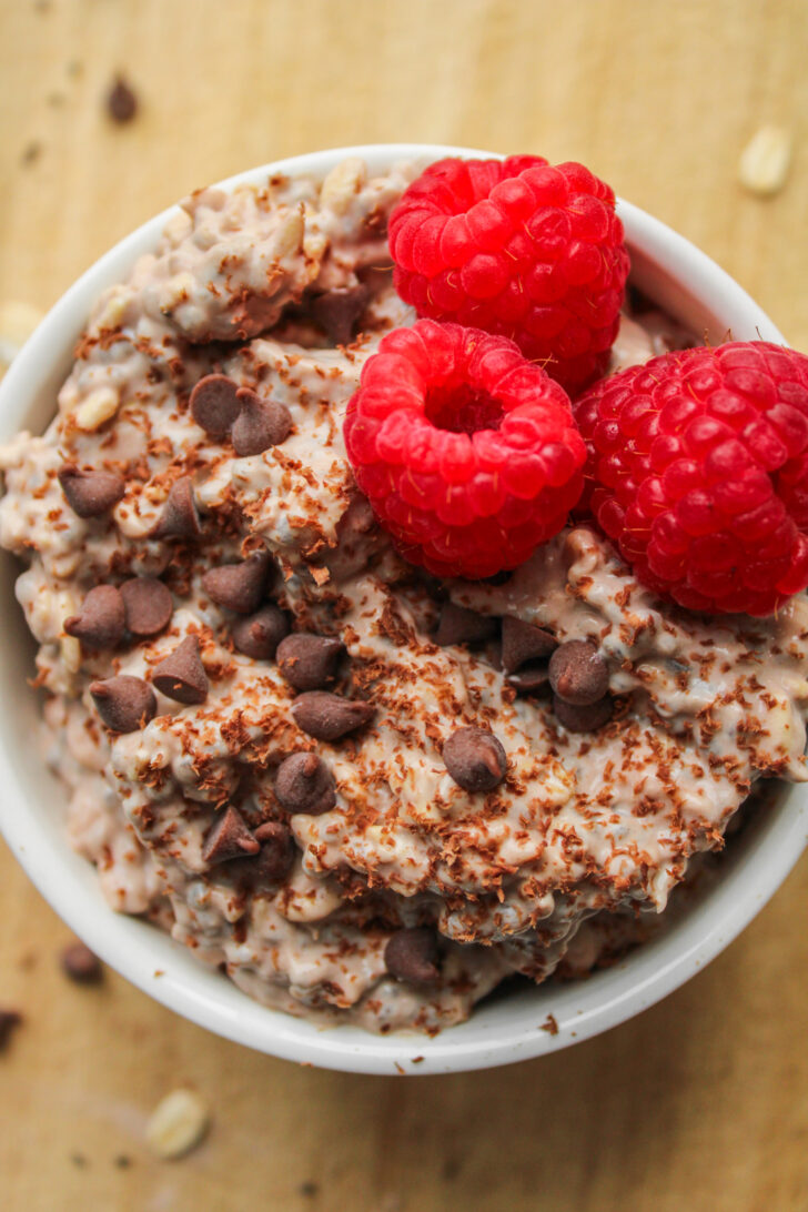 overhead shot of chocolate protein overnight oats topped with fresh raspberries and mini chocolate chips