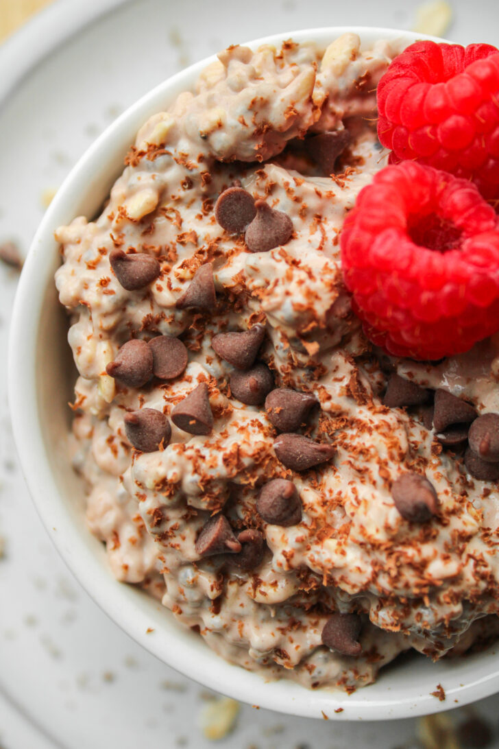 zoomed in overhead shot of chocolate protein overnight oats topped with fresh raspberries and mini chocolate chips