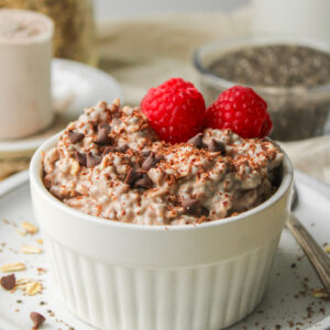 chocolate protein overnight oats, topped with chocolate chips and raspberries in a white ramekin dish