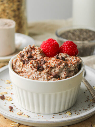 chocolate protein overnight oats, topped with chocolate chips and raspberries in a white ramekin dish