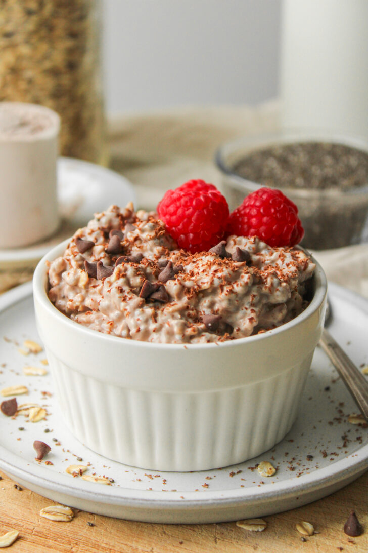 chocolate protein overnight oats, topped with chocolate chips and raspberries in a white ramekin dish