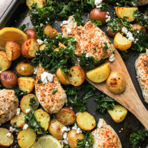 Mediterranean Sheet Pan Chicken Thighs and Potatoes with a wooden spatula picking up food