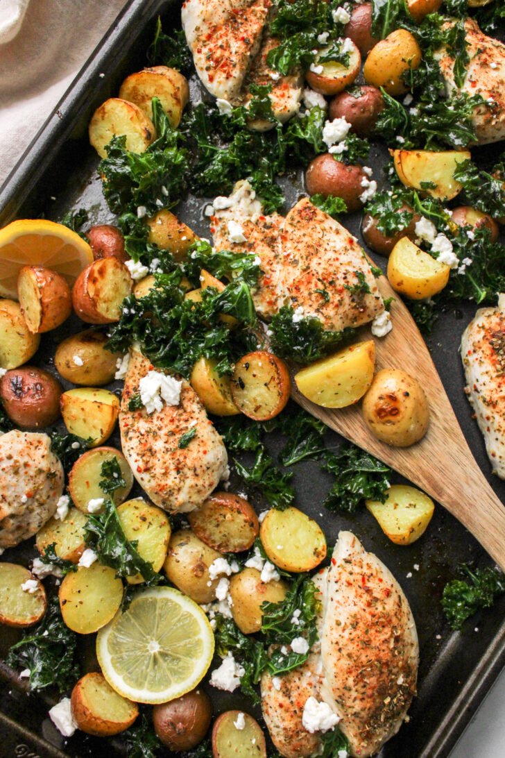 Mediterranean Sheet Pan Chicken Thighs and Potatoes with a wooden spatula picking up food