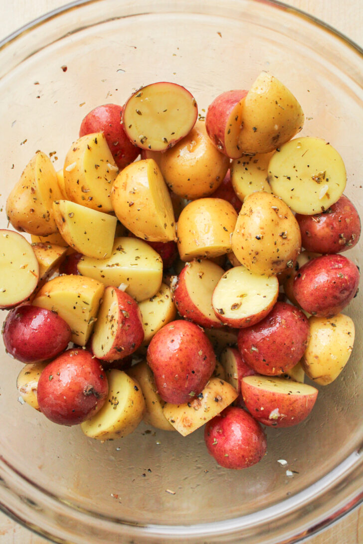 halved baby potatoes with seasoning in a glass bowl