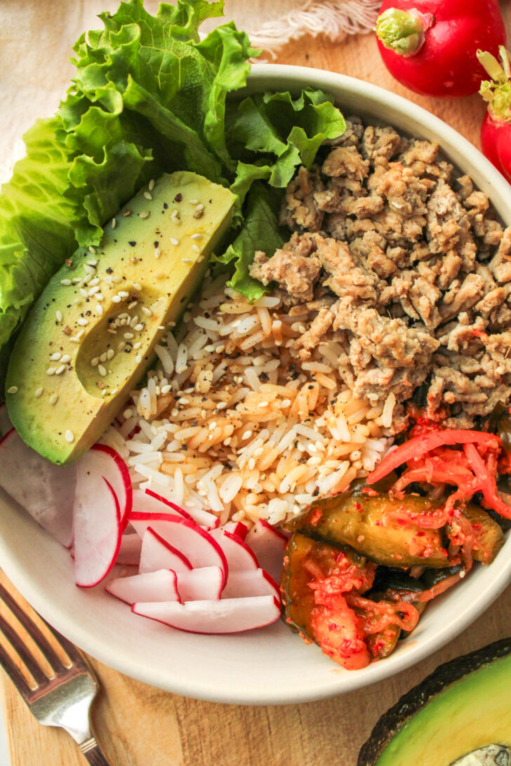 high protein kimchi rice bowls in a white ceramic bowl on top of a wooden cutting board